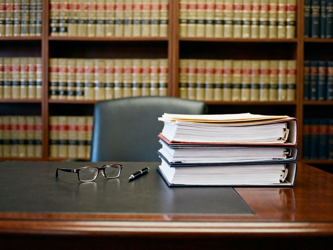 Schreibtisch einer Kanzlei mit Aktenstapel, Brille und Stift